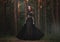 A beautiful gothic princess with pale skin and very long red hair in a black crown and a black long dress in a misty fairy forest.