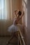 Beautiful graceful ballerina is practicing in the hall against the background of a window. Slender woman in tutu and