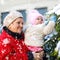 Beautiful grandmother holding baby girl in pram during snowfall in winter. Happy family. Carefree childhood and