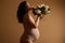 Beautiful gravid woman with big belly in pregnancy 28 week, wearing beige lingerie, posing with white blooming lilacs