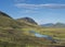 Beautiful green hills, lush grass and blue river with footbridge next to camping site on Alftavatn lake. Summer sunny