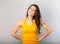 Beautiful grimacing confused serious woman with brown hair in casual yellow t-shirt looking up on grey background with empty copy