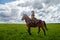 Beautiful gypsy girl on a horse in field with green glass in summer day and blue sky and white clouds background. Model in ethnic