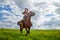 Beautiful gypsy girl rides a horse in field with green glass in summer day and blue sky with white clouds. Model in ethnic dress