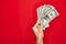 Beautiful hand of man holding bunch of dollar banknotes over isolated red background