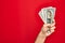 Beautiful hand of man holding bunch of dollar banknotes over isolated red background