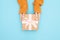 Beautiful hands of girl holding gift box present craft paper with pink bow, dressed in knitted sweater on blue