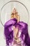 Beautiful happy blonde fancy woman in fashionable puffy purple dress with makeup and long curly hairstyle sitting in hanged bubble