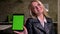 Beautiful happy caucasian blonde in swiping her tablet and demonstrating green screen at camera with calm charming smile