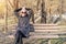 Beautiful happy caucasian  woman in jacket , hat and sunglasses enjoy  sitting on bench at city park or forest on sunny autumn day