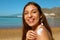 Beautiful happy cute woman applying suntan cream to her nose and shoulder with beach background