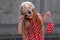 Beautiful happy girl in a red polka dot dress smiling on on concrete wall background. Cute joyful child with long hair