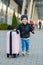 Beautiful happy girl travels with stylish suitcase. Little child traveler goes to the trip from airport.