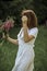 A beautiful happy girl in a white dress holds a bouquet of wild flowers in her hands. Portrait of a slender girl with a bouquet of