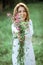 A beautiful happy girl in a white dress holds out a bouquet of wild flowers to the camera and smiles. Portrait of a slender girl