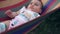 Beautiful happy little girl lying in a hammock in the garden and laughs