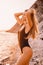 Beautiful happy woman in stylish swimwear on stones beach with warm sunset colors.