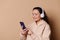 Beautiful happy woman in wireless headphones, testing new mobile application, scrolling playlist and listening to music