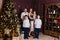 A beautiful happy young family of five stands in full height near the Christmas tree and look into the camera. mother, father and