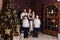 A beautiful happy young family of five stands in full height near the Christmas tree and look into the camera. mother, father and