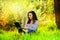 Beautiful happy young girl sits in a park on a glade with a laptop in green grass. sunny day