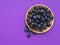 Beautiful healthy superfood blueberries on beautiful gold coloured plate on purple, violet with copyspace.