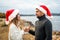 Beautiful heterosexual couple in love toasting outdoor wearing Santa Claus hat looking into each other`s eyes holding white wine