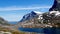 Beautiful high altitude mountains in Norway with snow on rocky peaks, a blue lake and wispy clouds in a blue sky on a sunny day.