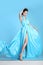 Beautiful High fashion woman in blue dress posing in studio. Glamour model in blowing chiffon dress. Stunning Woman in long