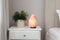 Beautiful Himalayan salt lamp and green houseplant on white stand in bedroom