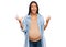 Beautiful hispanic woman expecting a baby showing pregnant belly crazy and mad shouting and yelling with aggressive expression and