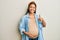 Beautiful hispanic woman expecting a baby, touching pregnant belly doing happy thumbs up gesture with hand