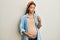 Beautiful hispanic woman expecting a baby, touching pregnant belly doing money gesture with hands, asking for salary payment,