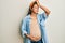 Beautiful hispanic woman expecting a baby, touching pregnant belly smiling confident touching hair with hand up gesture, posing