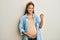 Beautiful hispanic woman expecting a baby, touching pregnant belly very happy and excited doing winner gesture with arms raised,