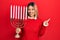 Beautiful hispanic woman holding menorah hanukkah jewish candle smiling happy pointing with hand and finger to the side