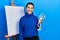 Beautiful hispanic woman with short hair holding manikin close to easel stand looking positive and happy standing and smiling with