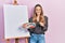 Beautiful hispanic woman standing drawing with palette by painter easel stand sticking tongue out happy with funny expression