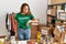 Beautiful hispanic woman wearing volunteer t shirt at donations stand checking the time on wrist watch, relaxed and confident