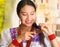 Beautiful hispanic woman wearing white blouse with colorful embroidery, using small hairbrush during makeup routine