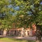 Beautiful historic building with salmon color plaster walls, behind green linden trees in summer.