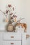 A beautiful homemade ginger cat and a Christmas bouquet in a ceramic vase on a white chest of drawers. Scandinavian style interior