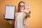 Beautiful inspector woman wearing glasses holding checklist clipboard over yellow background with open hand doing stop sign with