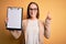 Beautiful inspector woman wearing glasses holding checklist clipboard over yellow background surprised with an idea or question