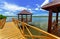 Beautiful inviting path trough the wooden bridge toward gazebo in tropical park against ocean and blue sky background