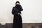 Beautiful Iranian girl in black dress and leather jacket. Attractive Muslim woman in hijab covering her face with a black scarf