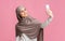 Beautiful islamic woman taking selfie on smartphone over pink background.
