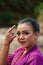 Beautiful Javanese woman with makeup and purple dress posing with her hand while sitting on the rock near the river