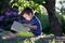 Beautiful kid boy, reading a book in garden, sitting next to a t