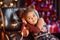 Beautiful kid girl 5-6 year old wearing stylish dress sitting in armchair over Christmas tree in room. Looking at camera. Holiday